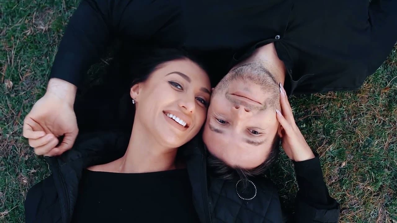 A couple lying on grass, heads together, both smiling at the camera
