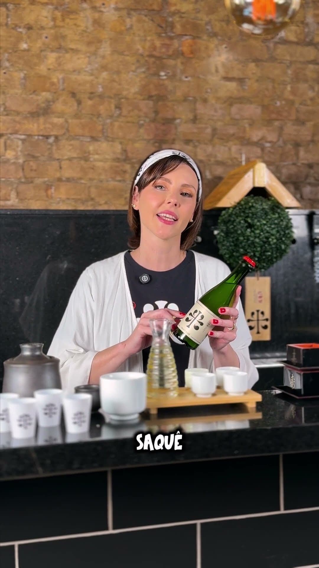 Patty presenting a bottle of sake behind a restaurant counter, with a burned-in caption reading SAQUÊ